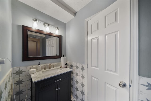 bathroom featuring a textured ceiling, vanity, a wainscoted wall, and tile walls