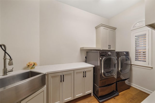 washroom featuring light wood-style flooring, a sink, washer and dryer, baseboards, and cabinet space