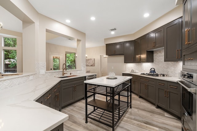 kitchen with light wood-type flooring, light stone counters, visible vents, appliances with stainless steel finishes, and a sink