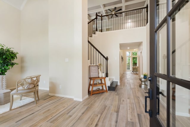 foyer entrance with baseboards, a ceiling fan, stairs, light wood-style floors, and coffered ceiling