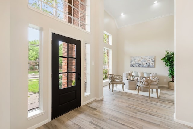 foyer entrance with light wood-style flooring, crown molding, a towering ceiling, and baseboards
