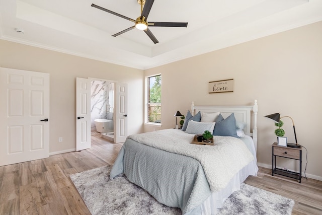 bedroom with baseboards, a raised ceiling, ornamental molding, light wood finished floors, and connected bathroom
