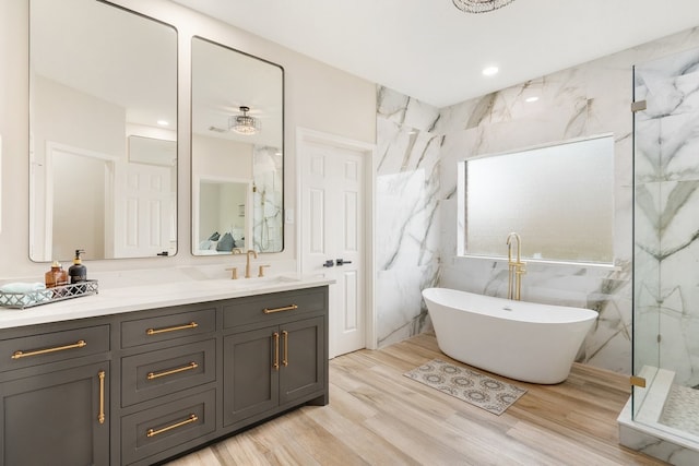 bathroom featuring vanity, recessed lighting, a marble finish shower, a freestanding bath, and wood finished floors