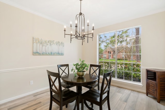 dining space with ornamental molding, baseboards, light wood finished floors, and a notable chandelier