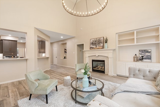 living area with built in features, baseboards, an inviting chandelier, a tiled fireplace, and light wood-style floors