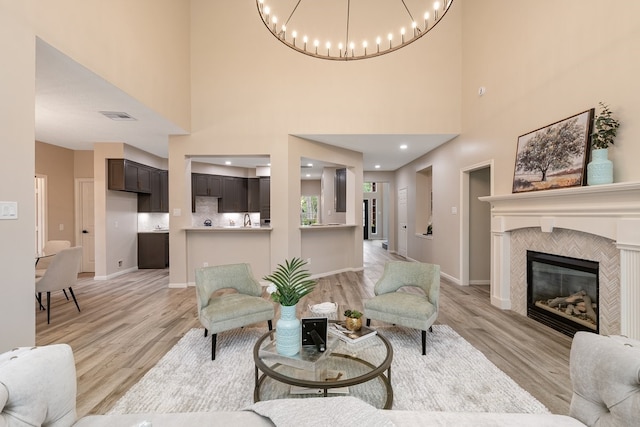 living room with light wood-type flooring, baseboards, a chandelier, a tiled fireplace, and visible vents