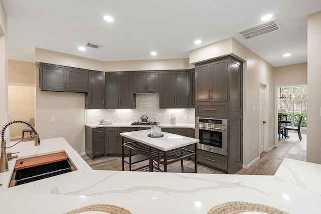kitchen featuring light stone countertops, visible vents, appliances with stainless steel finishes, a sink, and backsplash