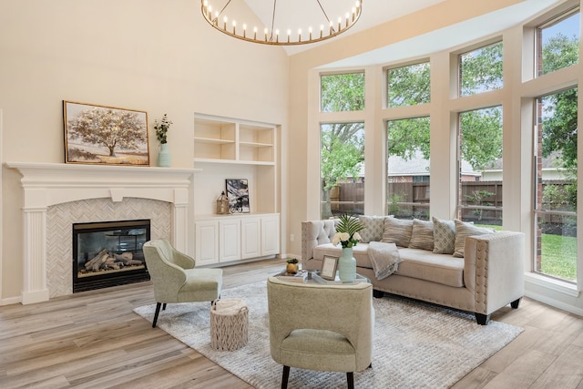 living area featuring a notable chandelier, a fireplace, a high ceiling, built in shelves, and wood finished floors