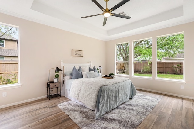 bedroom with a tray ceiling, wood finished floors, baseboards, and a ceiling fan