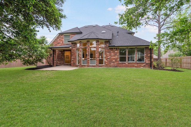 rear view of house featuring brick siding, fence, and a lawn