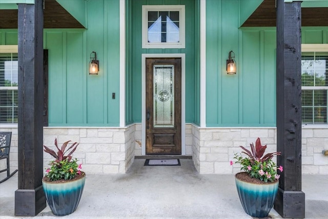 view of exterior entry featuring board and batten siding, covered porch, and stone siding