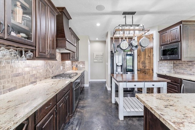 kitchen with dark brown cabinets, appliances with stainless steel finishes, concrete floors, baseboards, and custom range hood