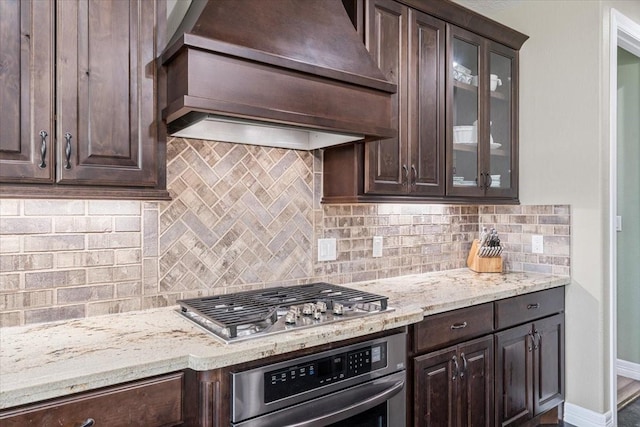 kitchen featuring stainless steel appliances, glass insert cabinets, premium range hood, and dark brown cabinets