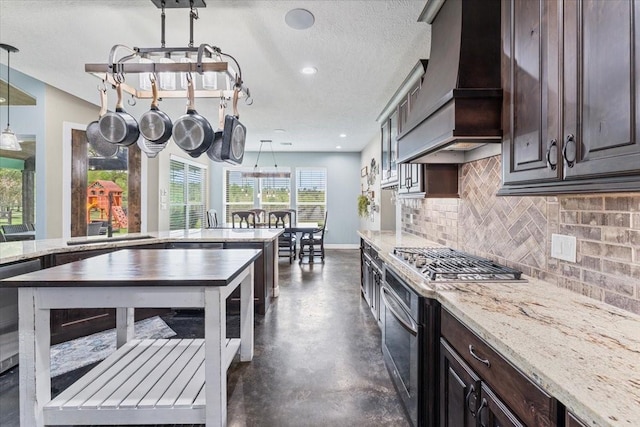 kitchen with concrete flooring, dark brown cabinets, tasteful backsplash, custom range hood, and stainless steel appliances