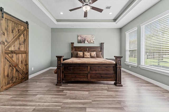 bedroom featuring a barn door, baseboards, wood finished floors, a tray ceiling, and visible vents