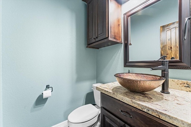 half bathroom with toilet, a textured wall, baseboards, and vanity