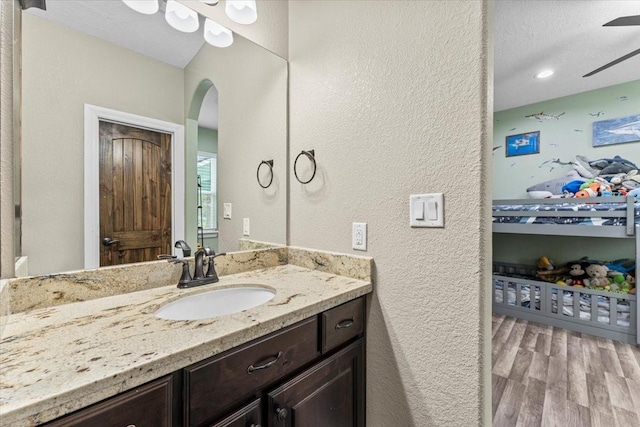 bathroom featuring vanity, a textured wall, ceiling fan, and wood finished floors