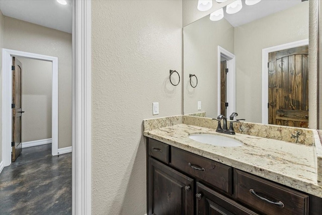bathroom with a textured wall, baseboards, finished concrete floors, and vanity