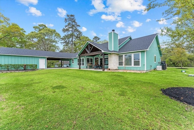 rear view of property with a shingled roof, a chimney, cooling unit, a carport, and a yard