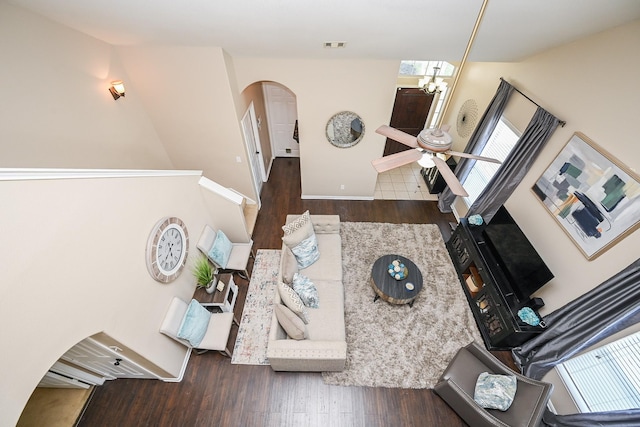 living area with wood finished floors, ceiling fan with notable chandelier, arched walkways, baseboards, and visible vents