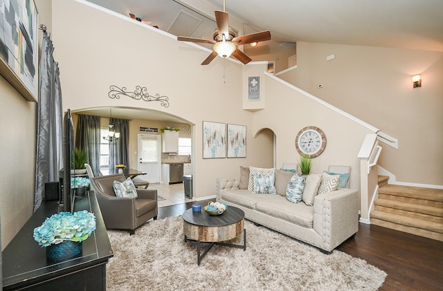 living room with arched walkways, wood finished floors, stairs, ceiling fan, and high vaulted ceiling