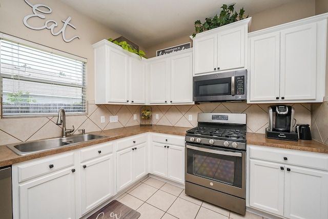 kitchen featuring tasteful backsplash, a sink, light tile patterned floors, stainless steel appliances, and white cabinets
