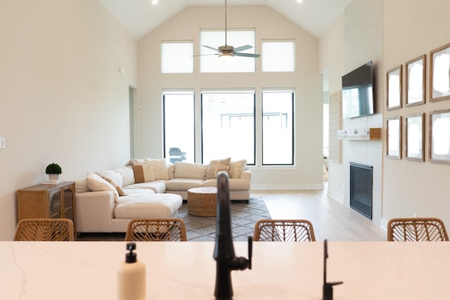 living area with a wealth of natural light, a tile fireplace, a ceiling fan, and light wood finished floors