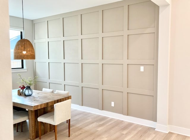 dining area featuring a decorative wall, light wood finished floors, and baseboards
