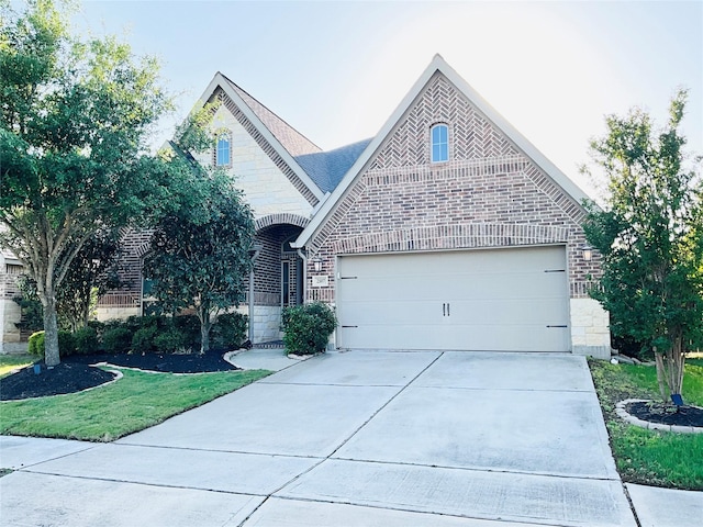french provincial home featuring an attached garage, brick siding, stone siding, a front yard, and concrete driveway