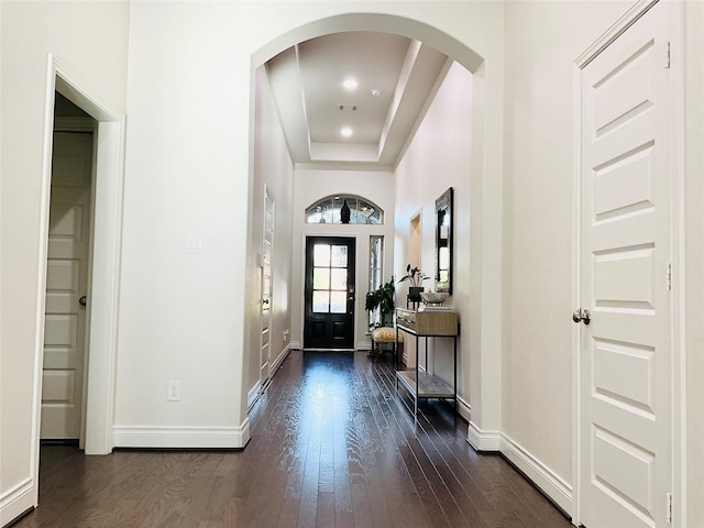 foyer entrance featuring arched walkways, baseboards, dark wood-style floors, and a raised ceiling