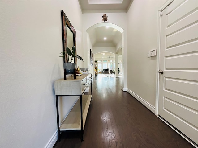 hallway featuring dark wood-type flooring, arched walkways, baseboards, and lofted ceiling