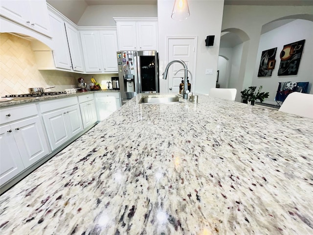 kitchen featuring appliances with stainless steel finishes, light stone counters, a sink, arched walkways, and white cabinetry