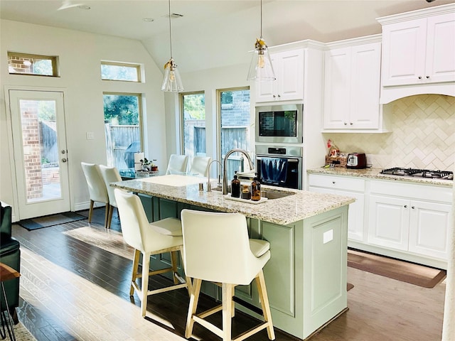 kitchen with light stone countertops, appliances with stainless steel finishes, a sink, decorative backsplash, and wood finished floors