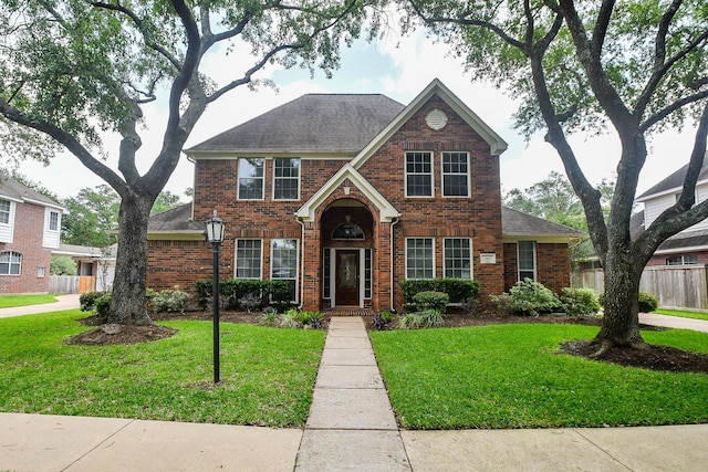 view of front of home with brick siding, fence, roof with shingles, and a front yard