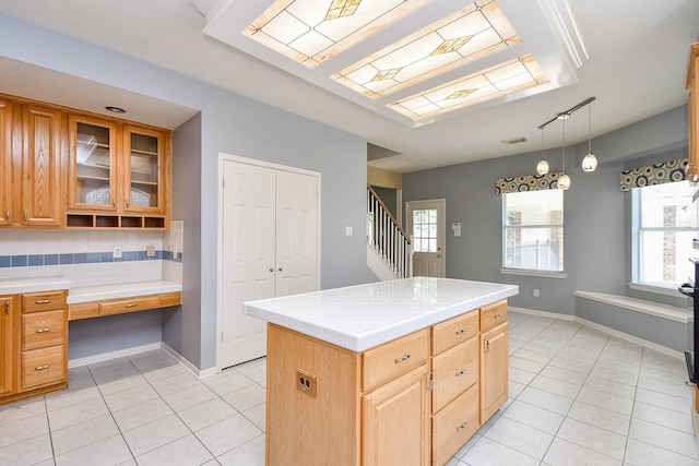 kitchen with glass insert cabinets, built in desk, light tile patterned floors, and plenty of natural light