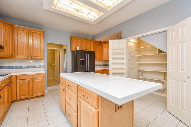 kitchen with decorative backsplash, tile counters, light tile patterned floors, and black fridge