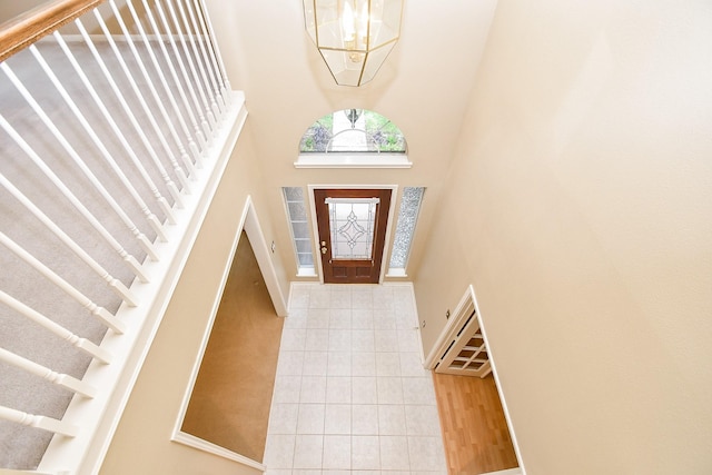 tiled entryway featuring stairway, a high ceiling, an inviting chandelier, baseboards, and visible vents