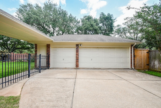 garage with a gate, concrete driveway, and fence