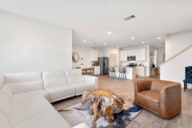 living room with visible vents, light wood-type flooring, recessed lighting, and stairs