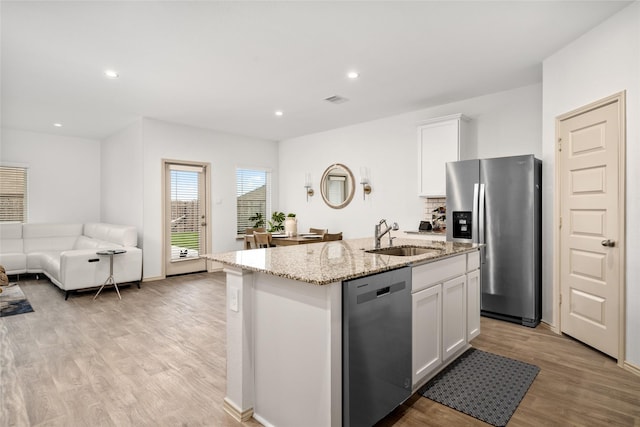 kitchen with open floor plan, white cabinets, a kitchen island with sink, stainless steel appliances, and a sink