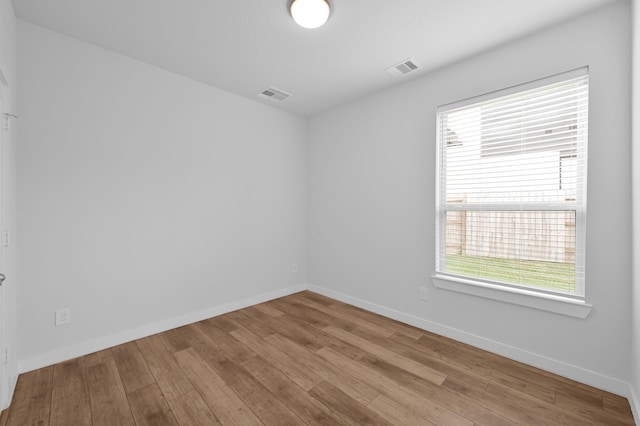 empty room with plenty of natural light, visible vents, baseboards, and hardwood / wood-style floors