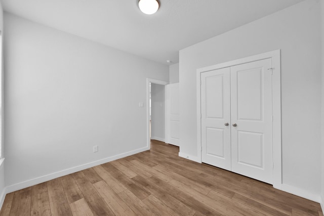 unfurnished bedroom featuring wood-type flooring, a closet, and baseboards