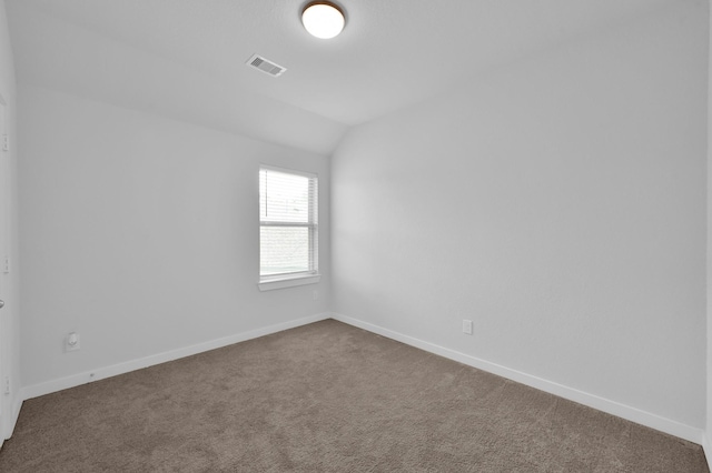 unfurnished room with vaulted ceiling, dark colored carpet, visible vents, and baseboards