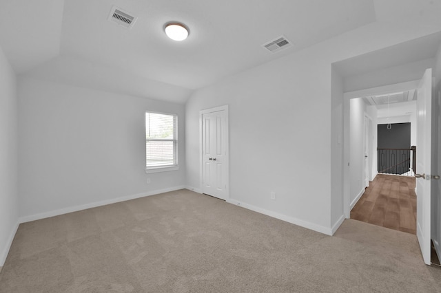 carpeted empty room with attic access, baseboards, vaulted ceiling, and visible vents