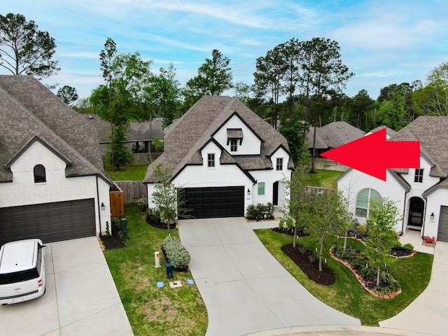 french country inspired facade featuring a garage, a shingled roof, a front lawn, and concrete driveway