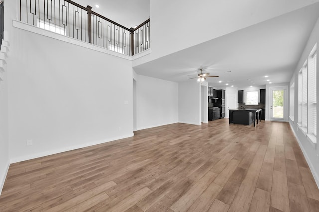 unfurnished living room featuring a ceiling fan, light wood-type flooring, a towering ceiling, baseboards, and recessed lighting