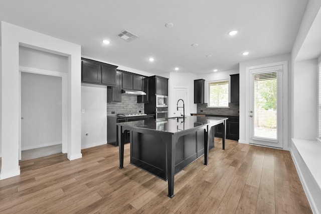 kitchen featuring stainless steel appliances, visible vents, decorative backsplash, dark cabinets, and under cabinet range hood