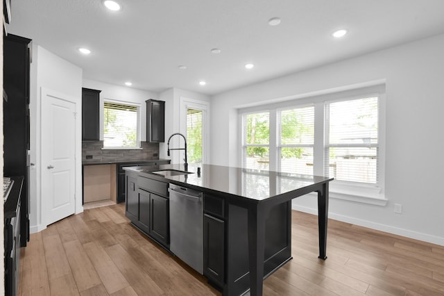 kitchen featuring a kitchen island with sink, a sink, dark countertops, dark cabinetry, and dishwasher