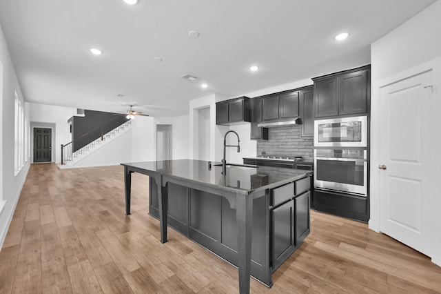 kitchen with light wood finished floors, a sink, tasteful backsplash, dark cabinets, and appliances with stainless steel finishes