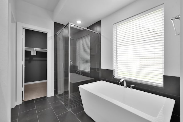 bathroom with tile patterned flooring, a freestanding tub, a spacious closet, and a stall shower